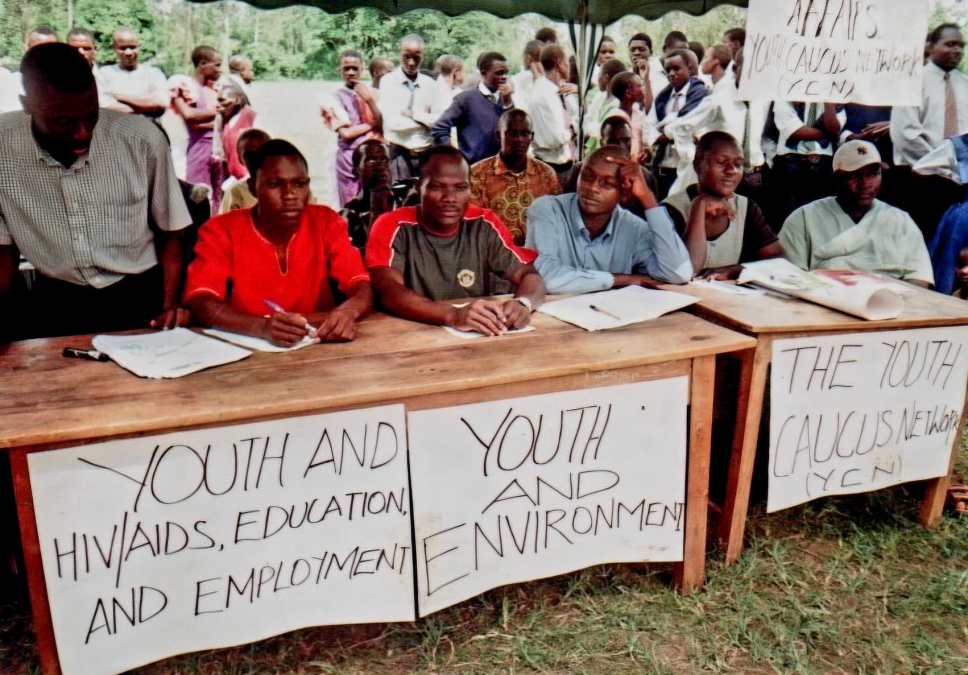 Young delegates seated at a table behind hand-written banners on youth and environment