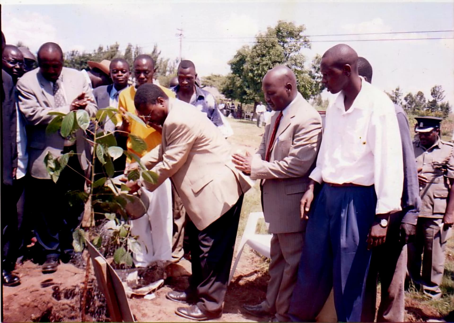 A guest watering a newly planted tree while colleagues steady him