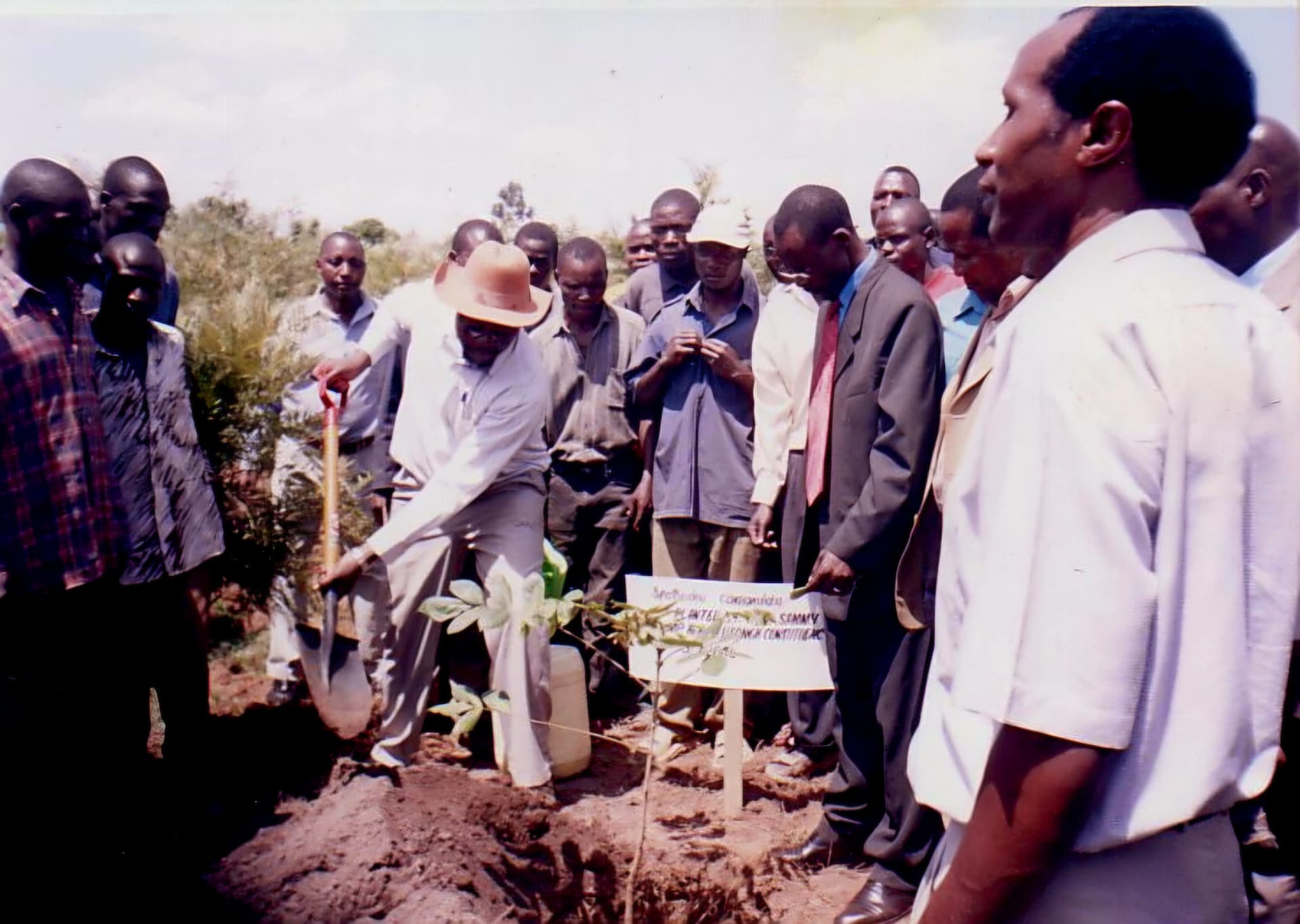 A guest planting a tree with a spade beside a hand-written commemorative marker