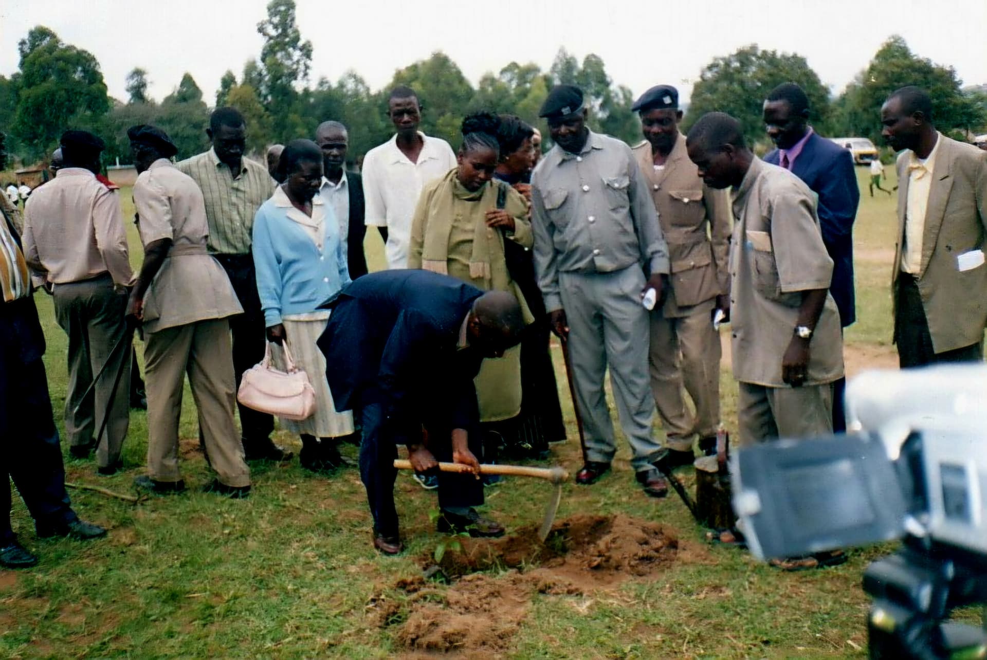 An official digging a planting hole with a hoe while officials and residents watch