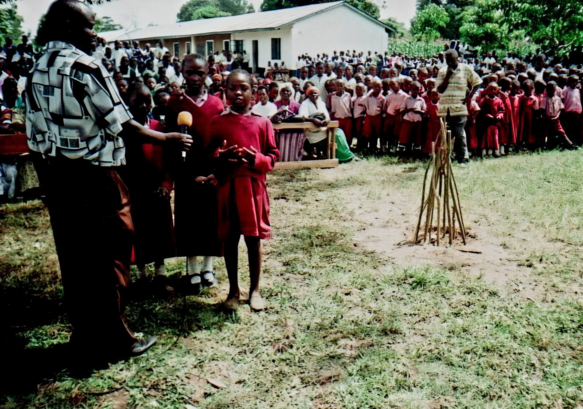 A pupil in red uniform speaking into a microphone before a large school assembly