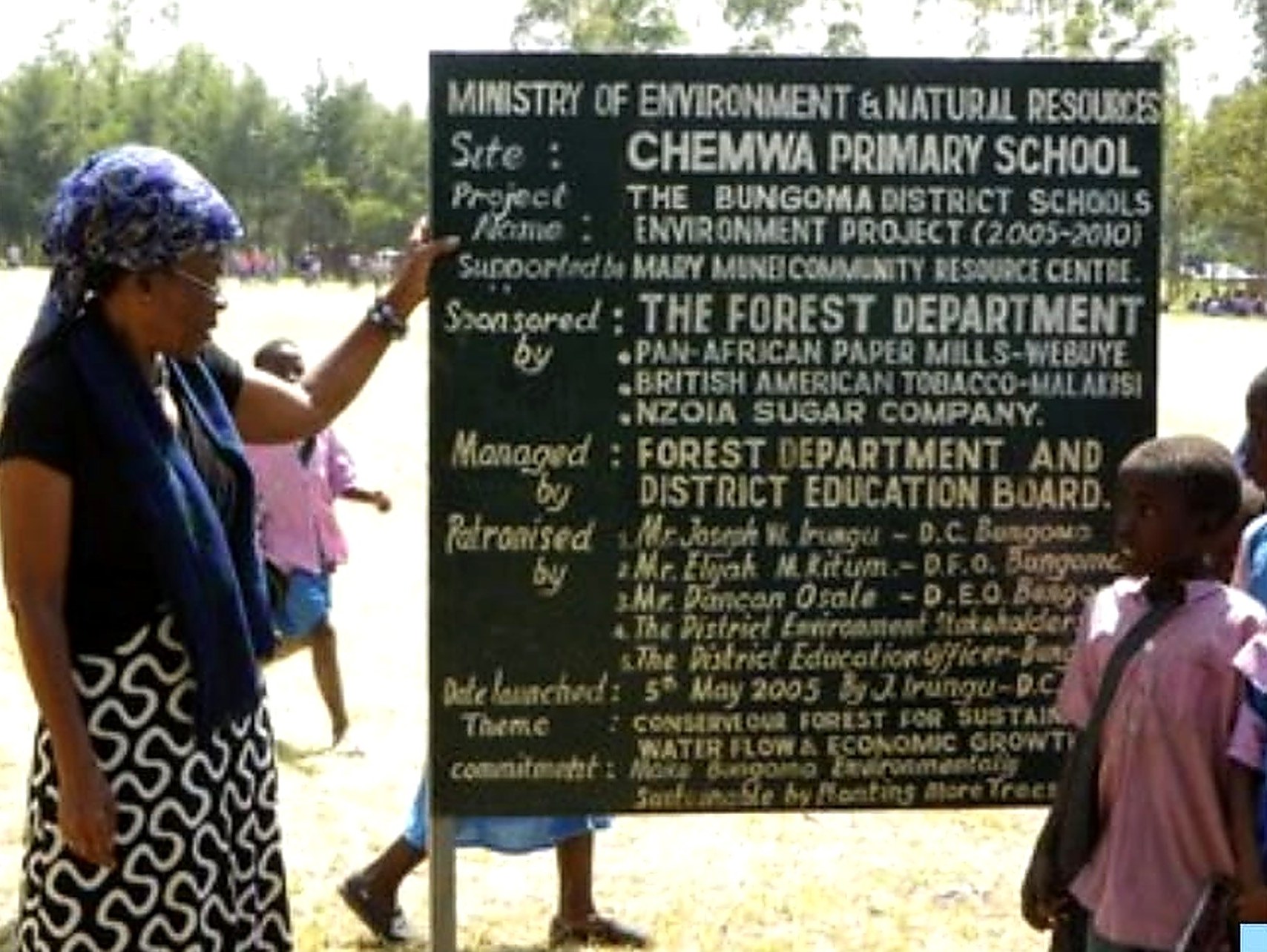 Alice Nabwera pointing at the Bungoma District Schools Environment Project signboard at Chemwa Primary School