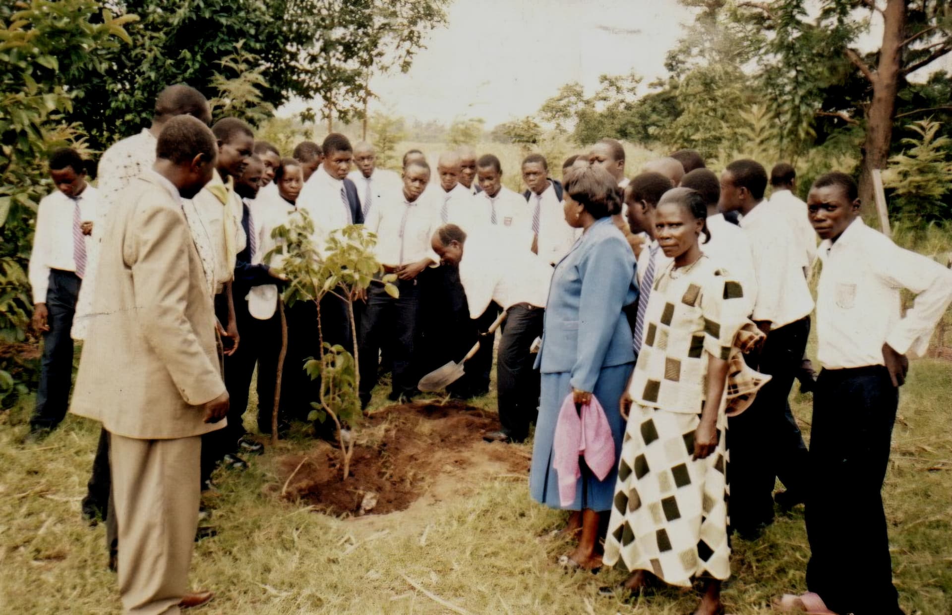 Secondary school students in uniform watching a tree being planted