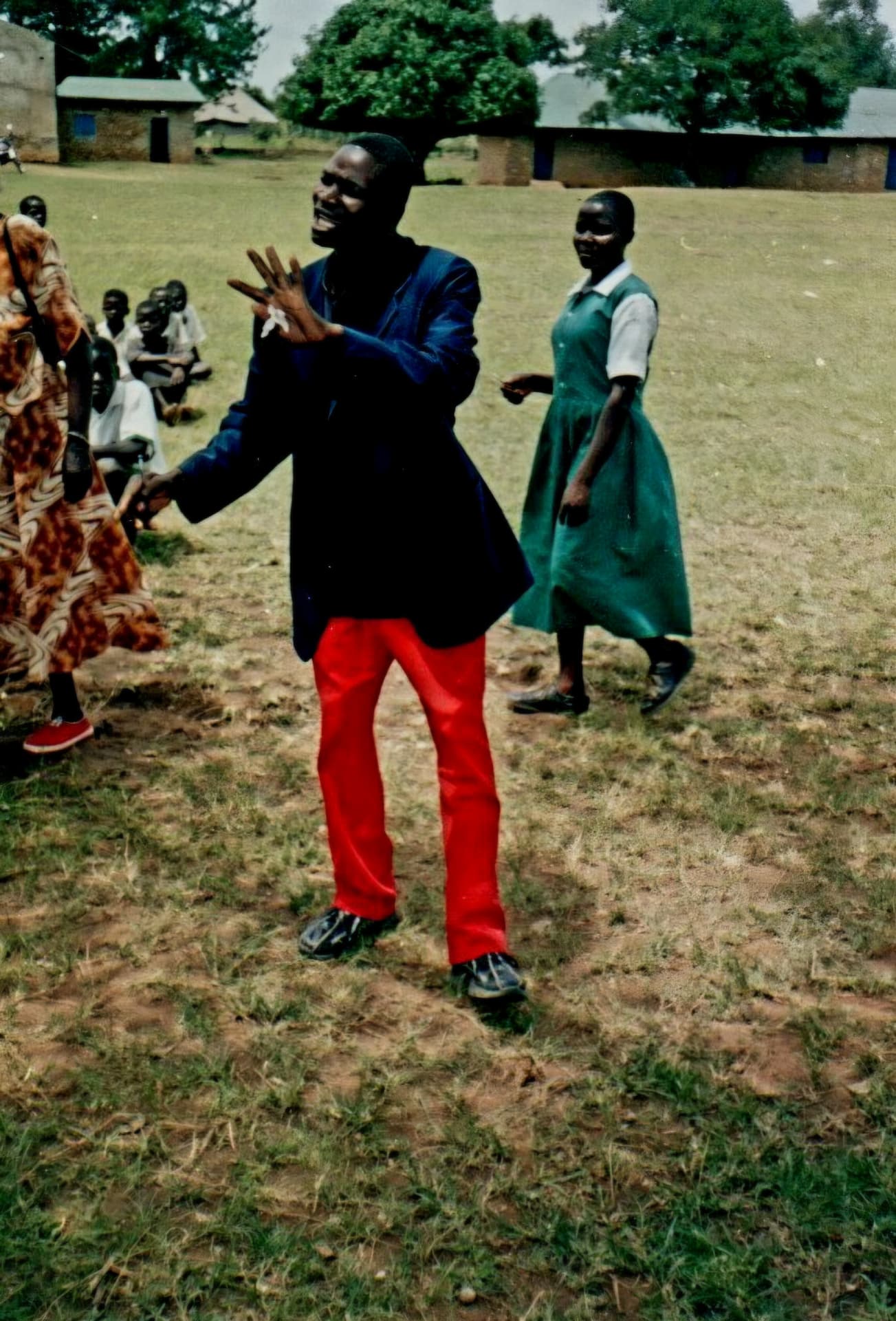 A man performing a dance on a school field with pupils watching