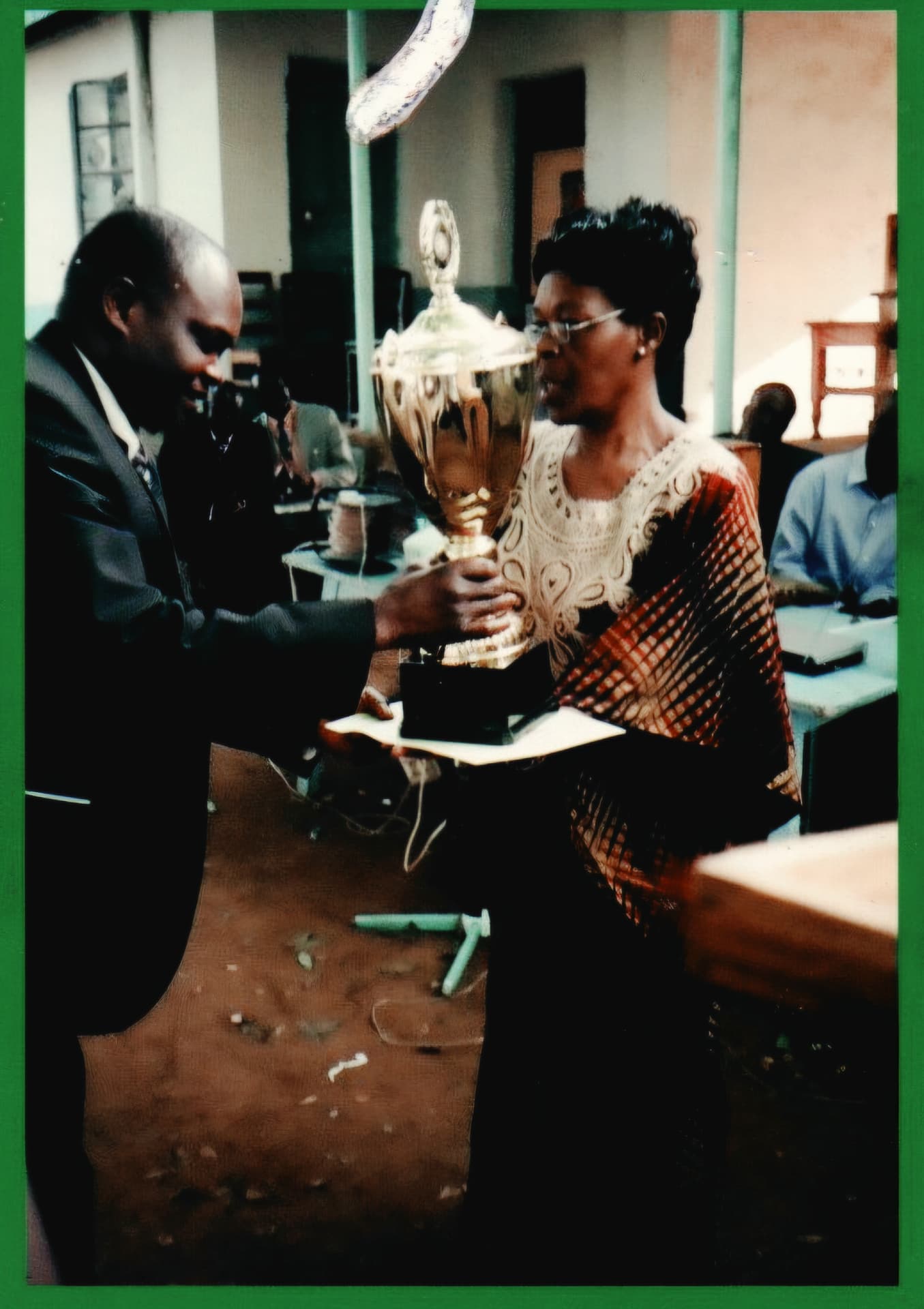 Alice Nabwera receiving a gold trophy from an official indoors
